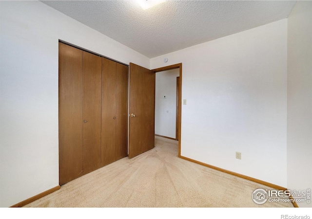 unfurnished bedroom with baseboards, a textured ceiling, a closet, and light colored carpet