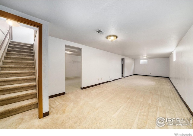 below grade area with stairway, baseboards, light colored carpet, and visible vents