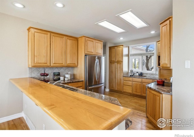 kitchen with freestanding refrigerator, backsplash, a sink, and light wood-style floors