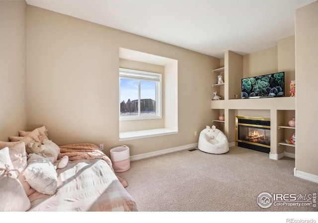 carpeted bedroom featuring baseboards and a glass covered fireplace