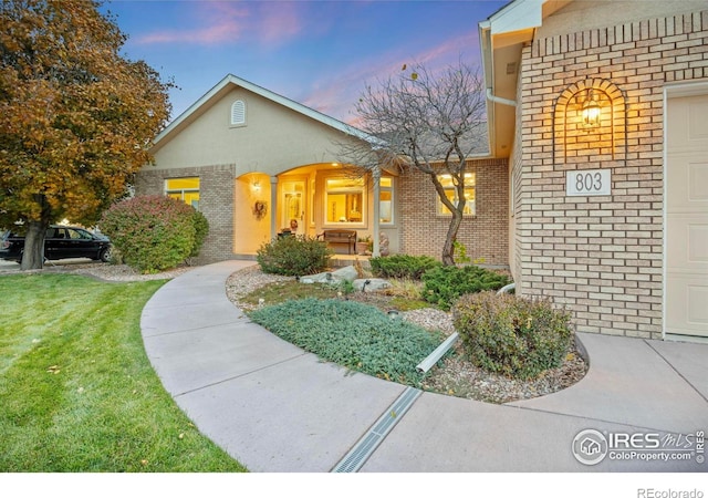 exterior entry at dusk with brick siding and a yard