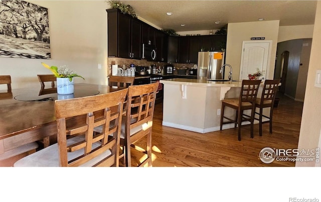 kitchen with a sink, stainless steel refrigerator with ice dispenser, light wood-style flooring, decorative backsplash, and dark cabinets