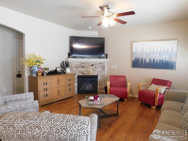 living area featuring a fireplace, ceiling fan, and wood finished floors