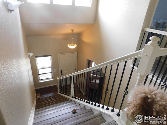 staircase with wood finished floors, baseboards, and a high ceiling