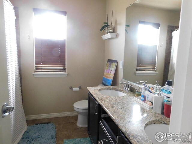 bathroom with toilet, double vanity, tile patterned flooring, and baseboards