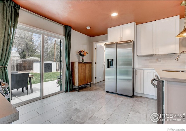 kitchen featuring stainless steel fridge, a sink, white cabinets, and light countertops