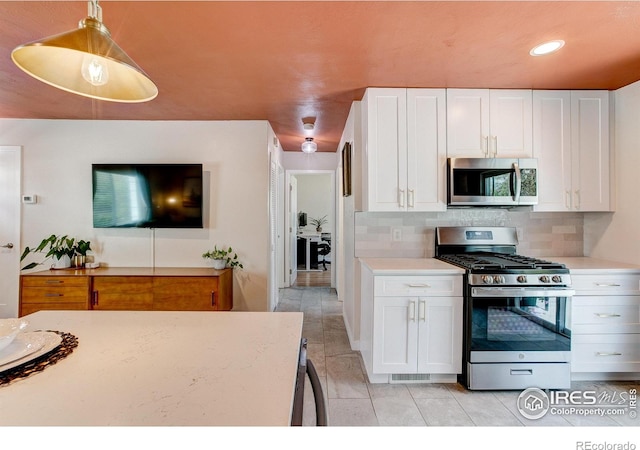 kitchen featuring white cabinets, light tile patterned flooring, stainless steel appliances, decorative light fixtures, and decorative backsplash