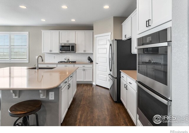 2121 Covered Bridge Pkwy, Windsor, CO 80550 - kitchen featuring decorative backsplash, dark wood-style floors, white cabinetry, a sink, and stainless steel appliances