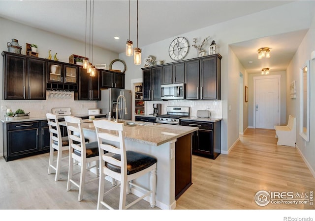 kitchen with backsplash, a kitchen bar, a sink, stainless steel appliances, and light wood-style flooring