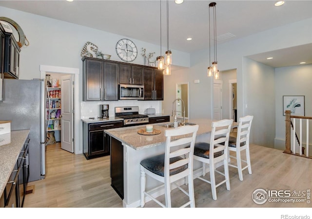 kitchen with appliances with stainless steel finishes, a sink, a kitchen breakfast bar, light wood-type flooring, and backsplash