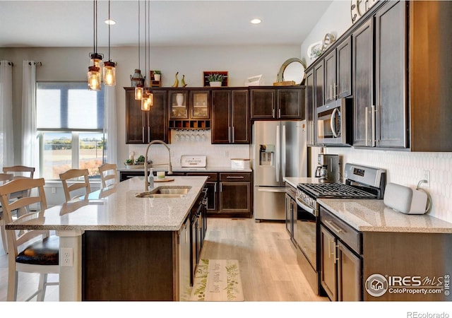 kitchen with decorative backsplash, appliances with stainless steel finishes, dark brown cabinets, a sink, and light wood-style flooring