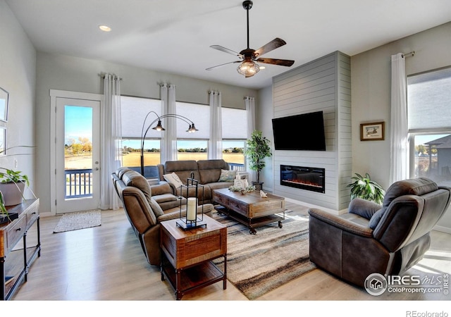 living room featuring a ceiling fan, a healthy amount of sunlight, light wood-style flooring, and a large fireplace