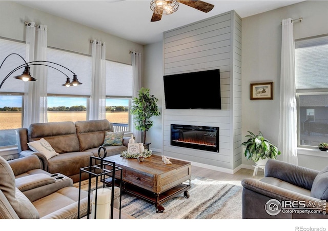 living room with a glass covered fireplace, baseboards, a ceiling fan, and wood finished floors