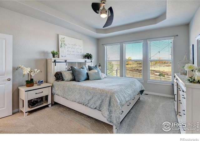 bedroom featuring a ceiling fan, baseboards, light colored carpet, and a tray ceiling