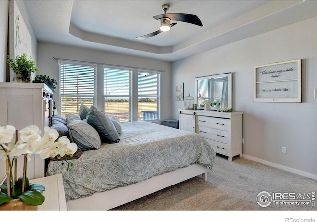 bedroom featuring baseboards, a ceiling fan, a raised ceiling, and light colored carpet