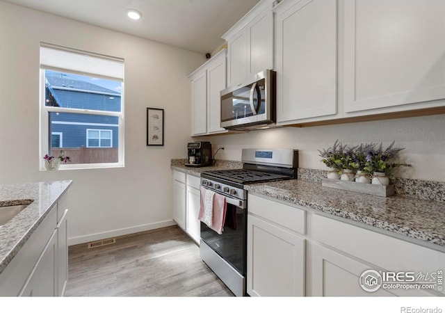 3759 Catmint St, Wellington, CO 80549 - kitchen featuring appliances with stainless steel finishes, light stone counters, light wood finished floors, white cabinetry, and visible vents