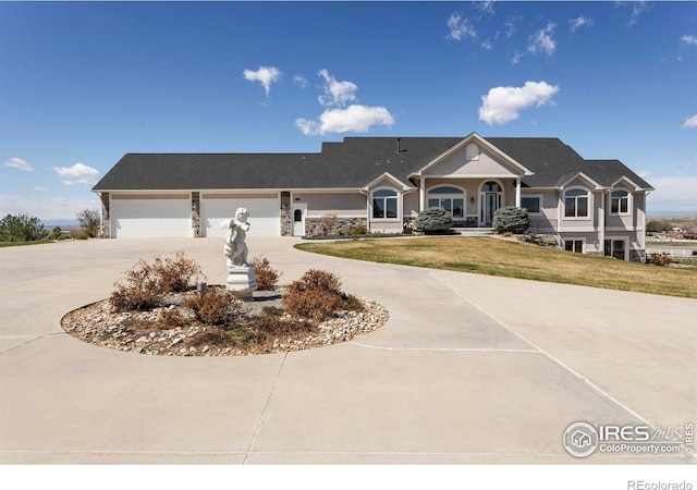 view of front of property with curved driveway, an attached garage, stone siding, and a front yard