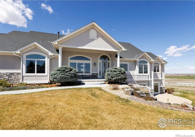 view of front of property featuring stucco siding, a front yard, and stone siding