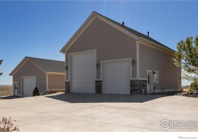 view of property exterior with a garage, driveway, stone siding, and stucco siding