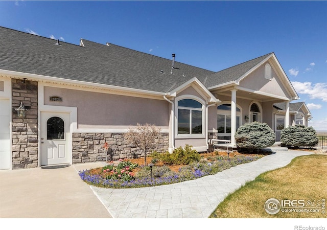 view of front of property featuring a shingled roof, stucco siding, and stone siding