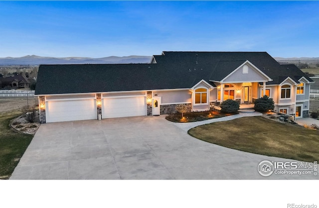 view of front of home with an attached garage, stone siding, a front yard, a mountain view, and concrete driveway