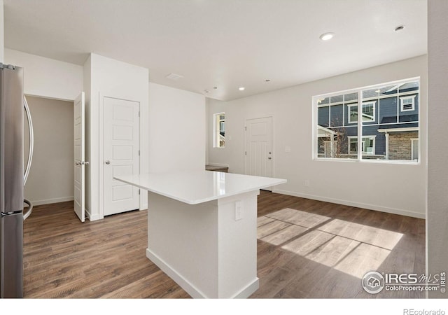 kitchen featuring freestanding refrigerator, a kitchen island, wood finished floors, and baseboards