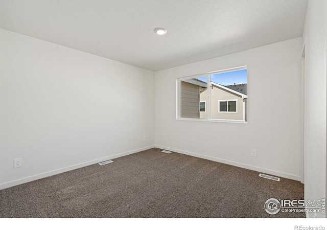 spare room with baseboards, dark colored carpet, and visible vents