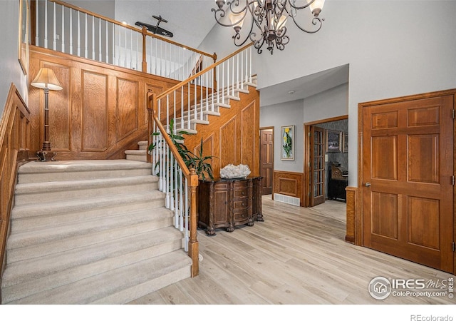 stairs with visible vents, wood finished floors, a high ceiling, a wainscoted wall, and a notable chandelier