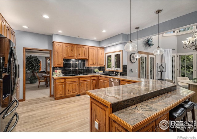 kitchen featuring light wood-style floors, a kitchen bar, brown cabinets, a sink, and black appliances