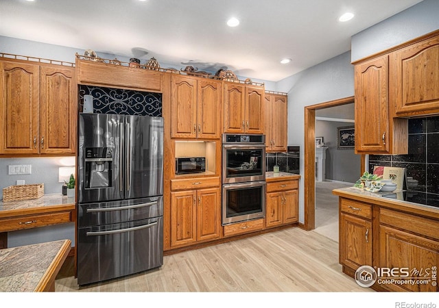 kitchen with brown cabinetry, light wood-style flooring, tile countertops, tasteful backsplash, and black appliances