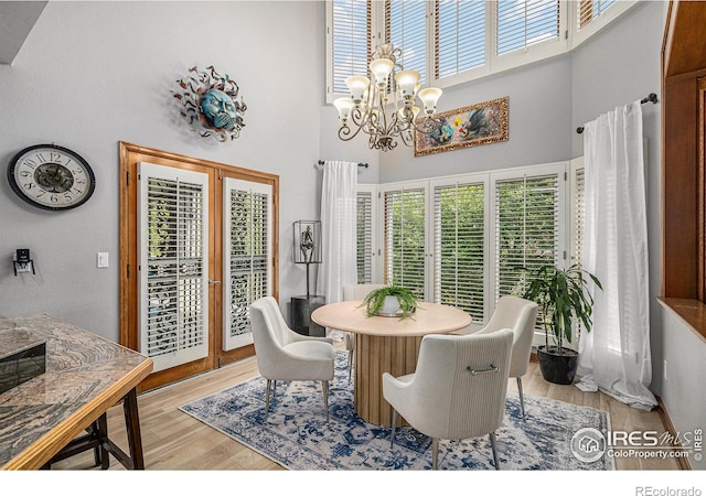 dining area featuring an inviting chandelier, light wood-style flooring, a high ceiling, and french doors