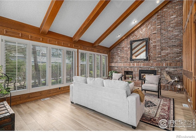 living room with visible vents, wood finished floors, a fireplace, beamed ceiling, and high vaulted ceiling