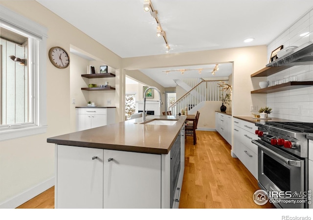 kitchen with open shelves, dark countertops, a sink, rail lighting, and high end stove