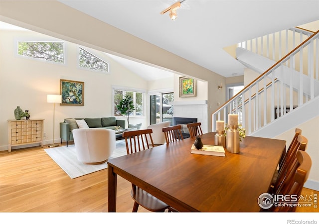 dining area featuring stairway, high vaulted ceiling, a fireplace, and wood finished floors