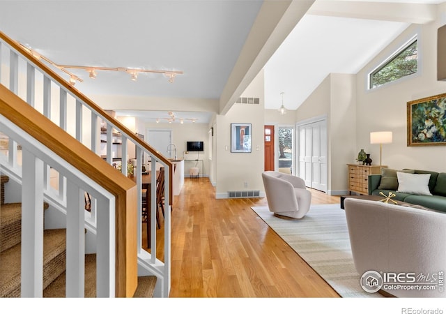 living room with plenty of natural light, visible vents, light wood-type flooring, track lighting, and stairs