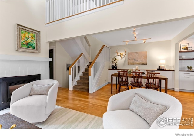 living area featuring light wood finished floors, a brick fireplace, rail lighting, baseboards, and stairway