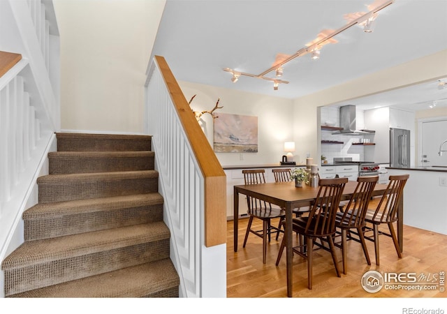 dining area with track lighting, light wood-style flooring, and stairs