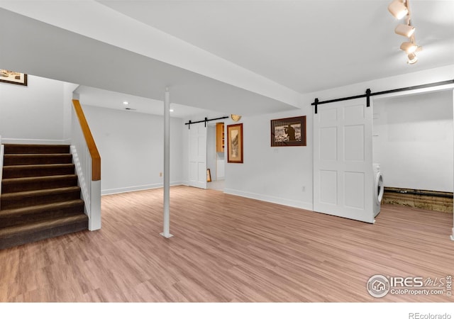 finished below grade area with stairway, light wood-style floors, washer / dryer, and a barn door