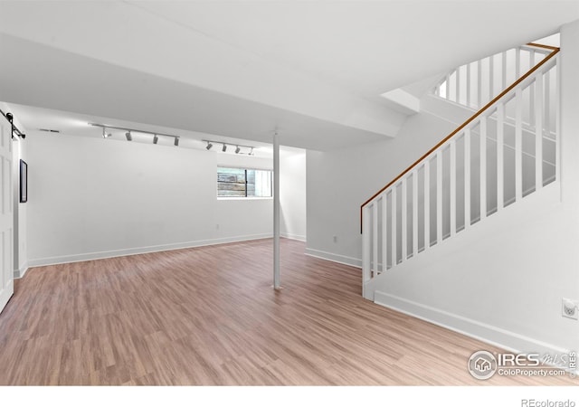 below grade area with stairs, baseboards, a barn door, and wood finished floors