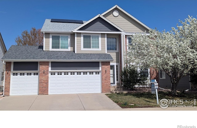 view of front facade with brick siding, an attached garage, roof mounted solar panels, and driveway
