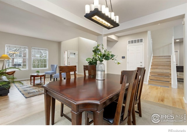 dining space featuring visible vents, light wood-type flooring, stairway, baseboards, and an inviting chandelier