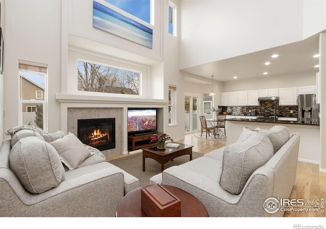 living room featuring a high ceiling, a fireplace, plenty of natural light, light wood-style flooring, and recessed lighting