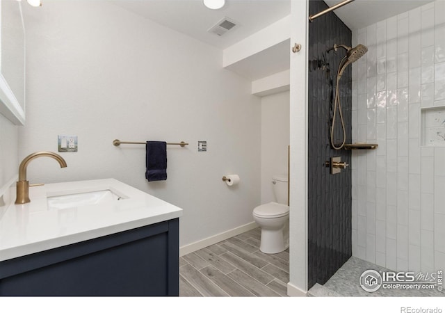 bathroom with a tile shower, a sink, toilet, wood tiled floor, and visible vents
