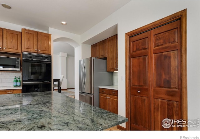 4866 Franklin Dr, Boulder, CO 80301 - kitchen featuring dobule oven black, brown cabinetry, arched walkways, tasteful backsplash, and freestanding refrigerator