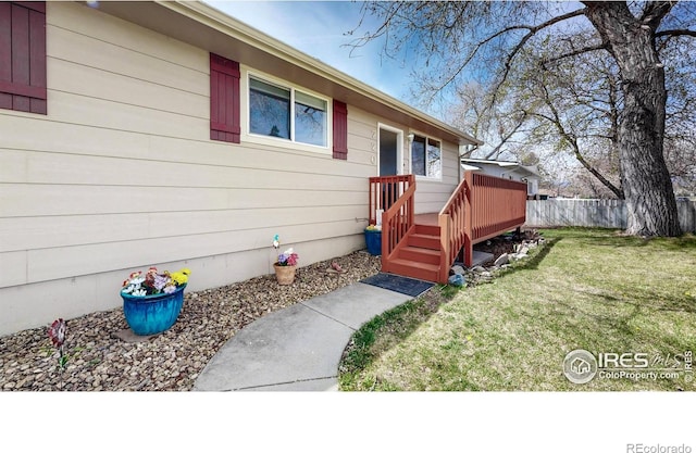 property entrance featuring a lawn, fence, and a deck