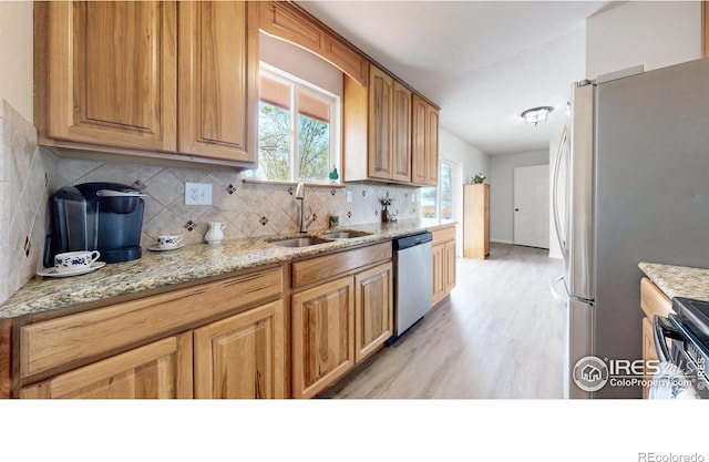 kitchen featuring light stone counters, tasteful backsplash, a sink, stainless steel appliances, and light wood-type flooring