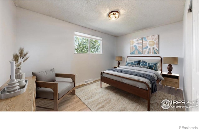bedroom featuring a textured ceiling, baseboards, visible vents, and wood finished floors