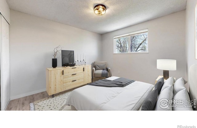 bedroom with a textured ceiling, baseboards, and light wood-style floors