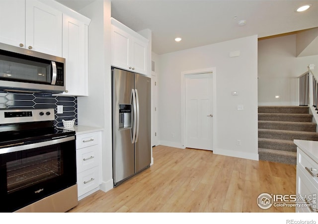 kitchen with appliances with stainless steel finishes, tasteful backsplash, light wood finished floors, white cabinets, and light countertops