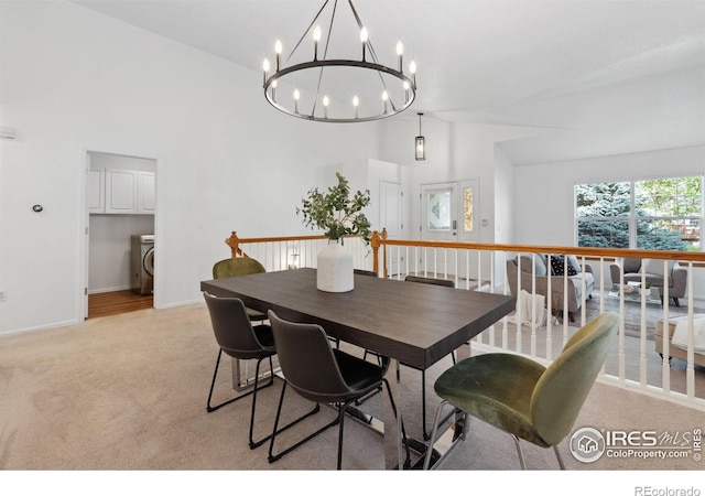 dining space featuring washer / dryer, baseboards, a high ceiling, light colored carpet, and a chandelier